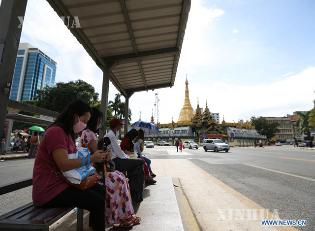 ရန်ကုန်မြို့ရှိ ဘတ်စ်ကားမှတ်တိုင်တစ်ခု တွင် ကားစီးရန် စောင့်ဆိုင်းနေသော ပြည်သူများအား တွေ့ရစဉ်(ဆင်ဟွာ)