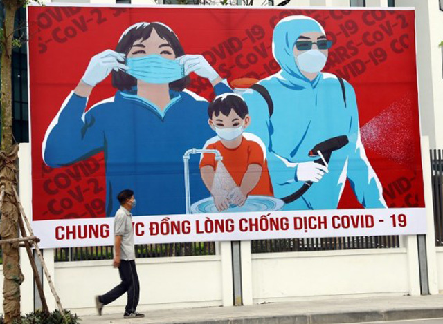 ဗီယက်နမ်နိုင်ငံ ဟနွိုင်းမြို့၌ COVID-19 ရောဂါတိုက်ဖျက်ရေး ပိုစတာရှေ့တွင် လမ်းလျှောက်နေသူတစ်ဦးအား တွေ့ရစဉ်(VNA/Handout via Xinhua)